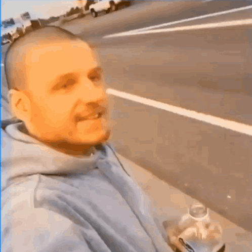 a man with a shaved head is taking a selfie on the side of the road