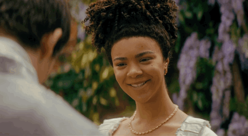 a woman wearing a pearl necklace is smiling at a man