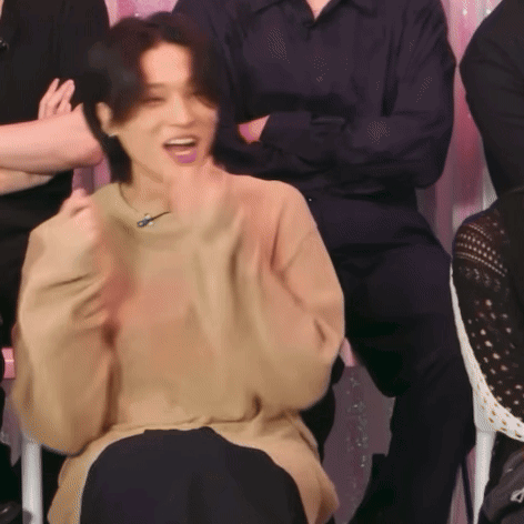 a woman in a tan sweater is sitting in front of a group of people and laughing