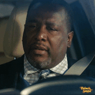 A man in a car gives a weary, upset look from behind the steering wheel.