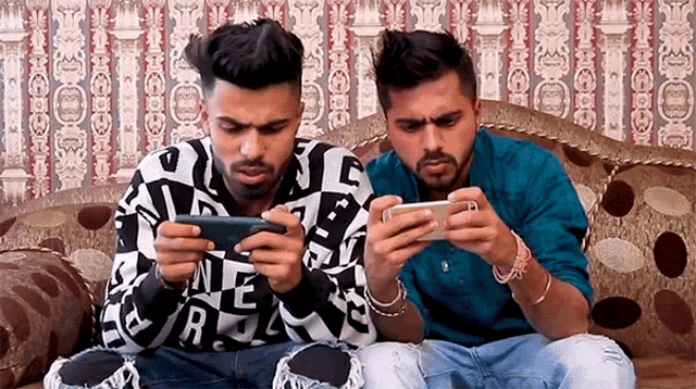 two men sitting on a couch playing a game on their cell phones