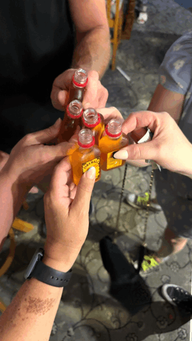a group of people are toasting with small bottles of hot sauce with a yellow label