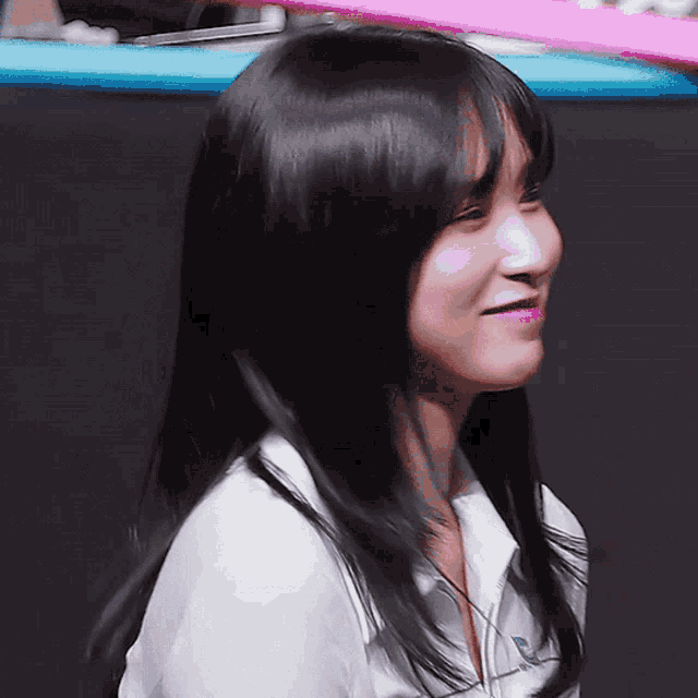 a woman with long black hair is smiling and wearing a white shirt with the letter r on the front