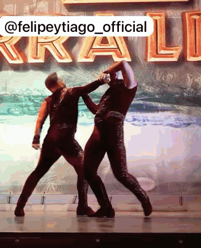 a couple of dancers are dancing in front of a sign that says @felipetytiago_official