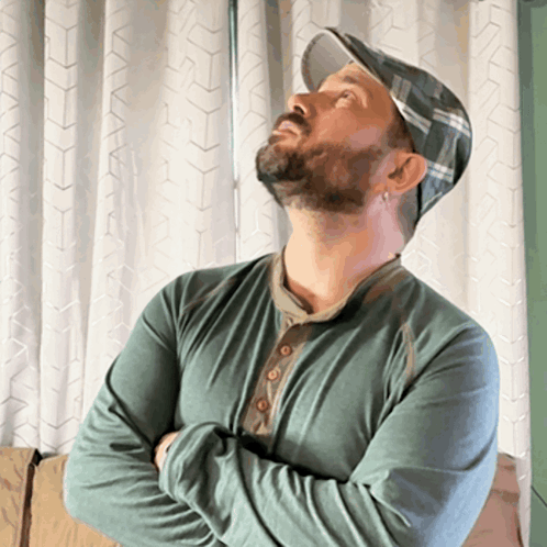 a man wearing a hat and a green shirt looks up at something