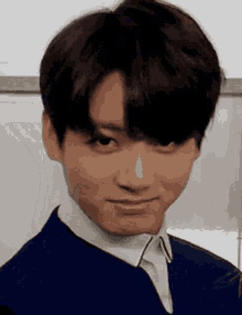 A man in formal blue clothing looks up with a mischievous smirk.
