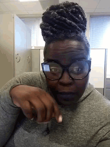 a man wearing glasses and dreadlocks is pointing at something