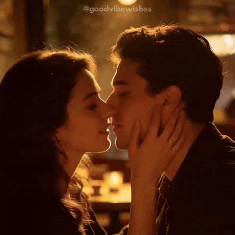 A couple kiss warmly in a softly lit restaurant or bar.