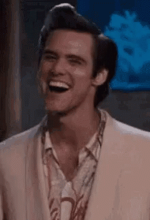 Jim Carrey smiles broadly in a pale suit.