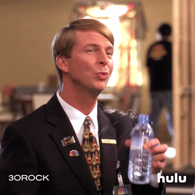 A man in a suit shakily holds a bottle of water with a nervous smile.