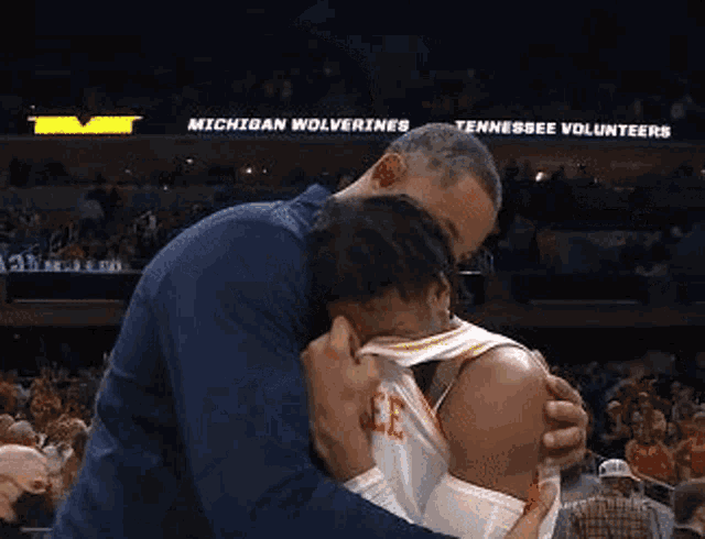 a man is hugging a basketball player in a stadium .