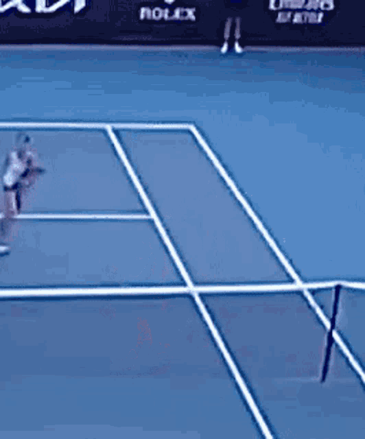 a woman is playing tennis on a blue court with a rolex sign in the background