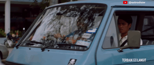 a man is driving a blue van with a sticker on the windshield that says ' astroshaw ' on it