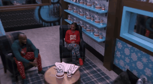 a woman wearing a merry christmas sweater sits in a chair next to a man