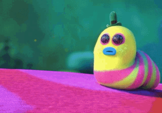 a colorful stuffed animal with a hat on its head is sitting on a purple surface .