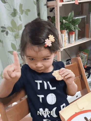 A small child at a dining table wags a finger and shakes their head no.