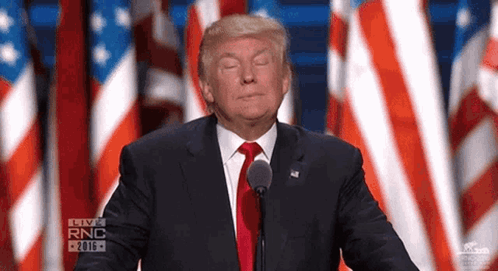 Donald Trump stands at a podium in front of American flags with a puzzled expression.