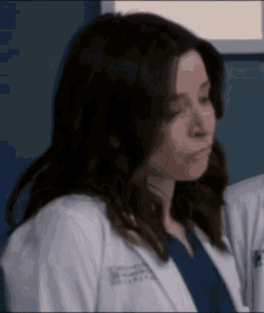 a close up of a woman wearing a white lab coat and a blue scrub top