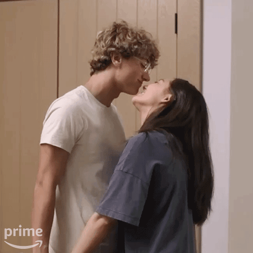 A tall man and woman lean toward each other in a softly lit room.
