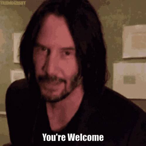 Keanu Reeves looks toward the camera with a faint smile in a dim indoor scene.