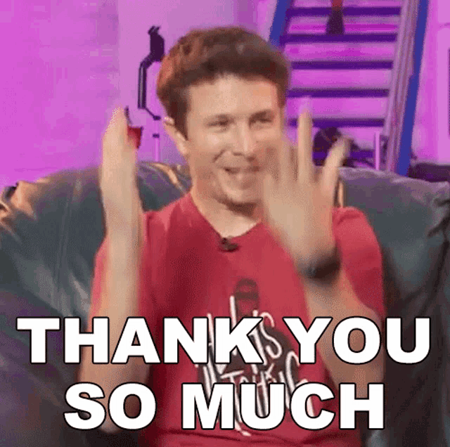 a man in a red shirt is sitting on a couch with his hands in the air and says " thank you so much "