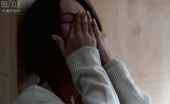 A woman covers her face with both hands in a dark emotional scene.