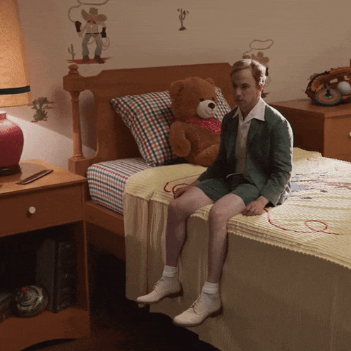 a man sits on a bed with a teddy bear on it