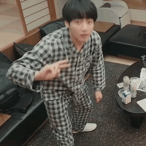 A man in plaid pajamas gestures upward in a kitchen or dining area.