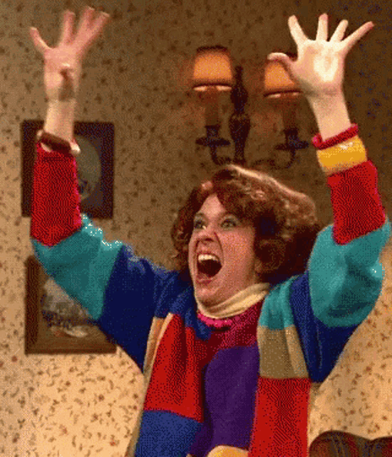 A person in a colorful jacket raises both hands in an ecstatic reaction.