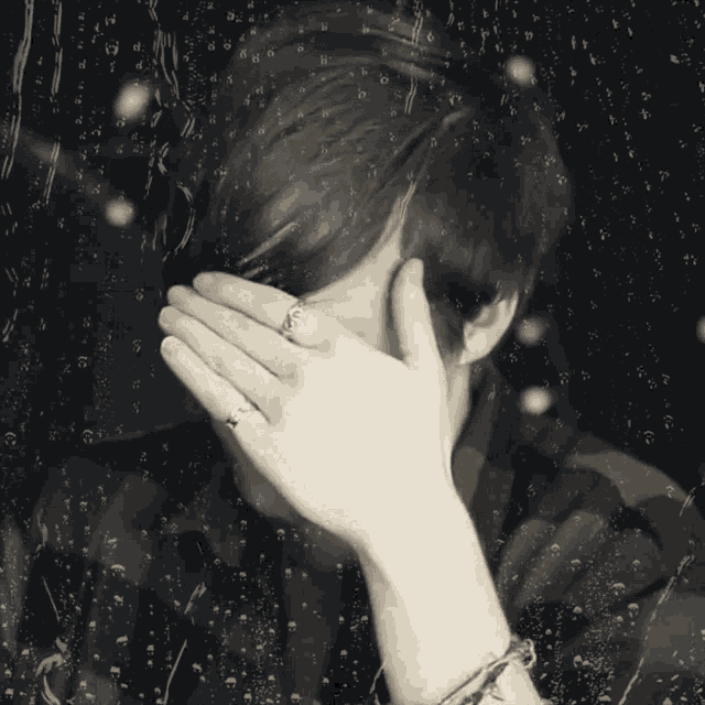 a person covering their face with their hands in front of a window with water drops on it