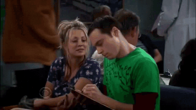 a man in a green shirt is writing on a clipboard while a woman sits next to him