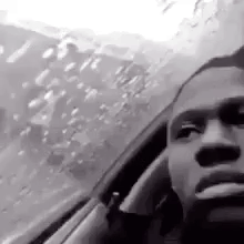 A person appears distressed in a grainy black-and-white close-up from inside a vehicle.