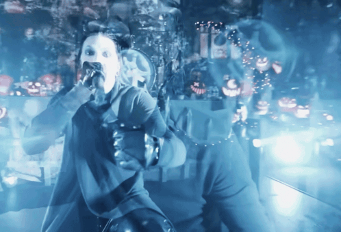 a woman singing into a microphone in a dark room with ghosts and pumpkins in the background