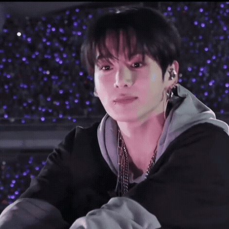 A man in a black jacket smiles softly against a purple starry backdrop.
