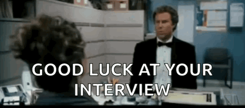 a man in a tuxedo is sitting at a desk talking to another man in an office .