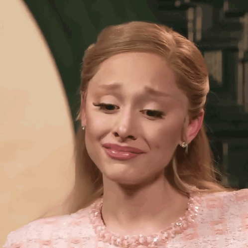 A woman in a pink dress makes a teary, uneasy expression.