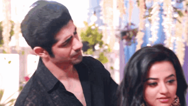 a man in a black shirt looks at a woman in a black dress