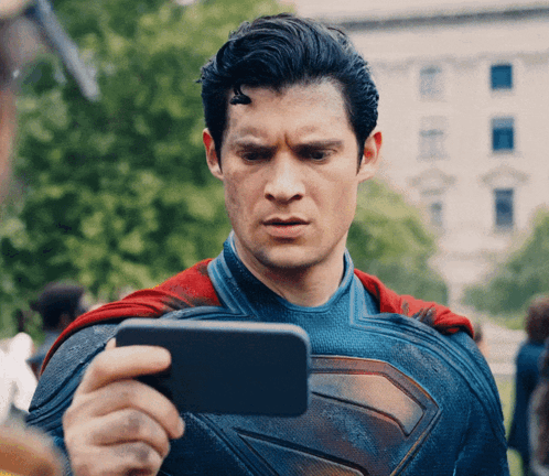 Superman in a blue suit looks down at a phone with concern.