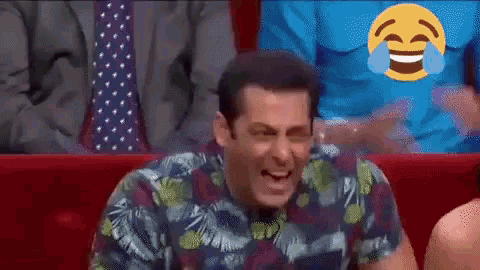 a man in a floral shirt is laughing with tears coming out of his eyes while sitting in a theatre .