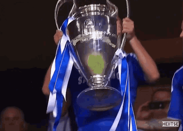 a man in a blue shirt is holding a trophy with the word heitse on the bottom