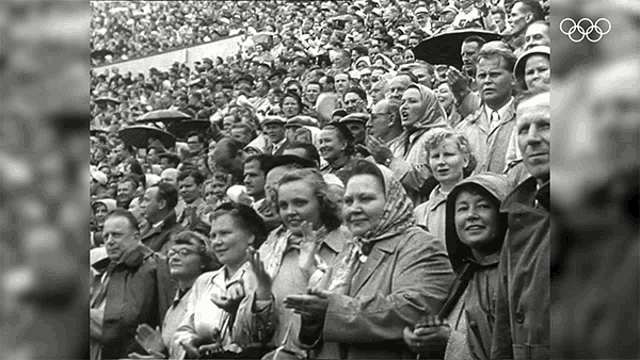 a black and white photo of a crowd of people with the olympic logo in the background
