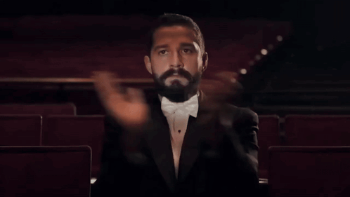 A tuxedoed man claps alone in a theater.