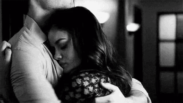 A black-and-white couple embraces in a dim room.