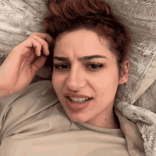a woman laying on a bed with her hand in her hair making a funny face