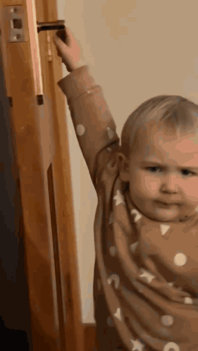 a baby is reaching for a door handle and making a face .