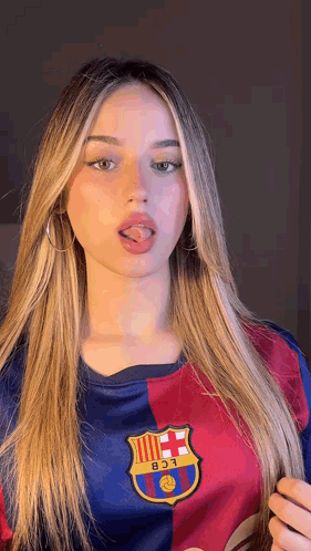 a young woman wearing a barcelona jersey is sticking her tongue out .