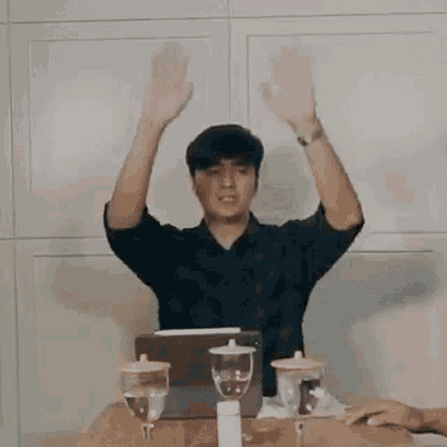 a man is sitting at a table with his hands in the air and a laptop .