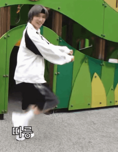 a man in a white jacket and black shorts is jumping in front of a green building with korean writing on it