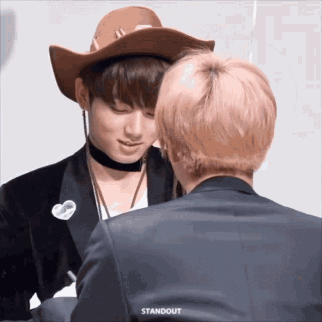 Two men face each other closely, one in a cowboy hat, in a playful scene.