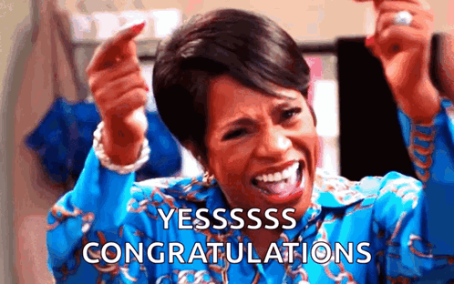 A smiling woman in a blue patterned outfit raises her hands with “YESSSSS CONGRATULATIONS.”